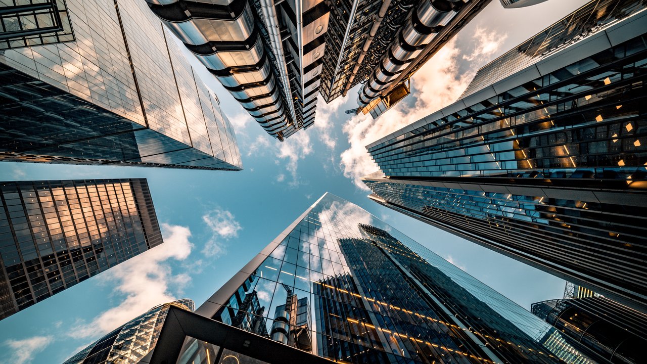 View of tall modern skyscrapers from ground level, reflecting clouds and blue sky.