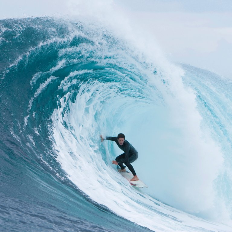 Person riding surfboard inside curl of wave